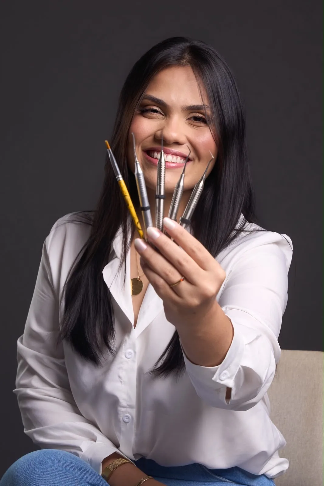 Karen Brandão sorrindo, segurando instrumentos odontológicos